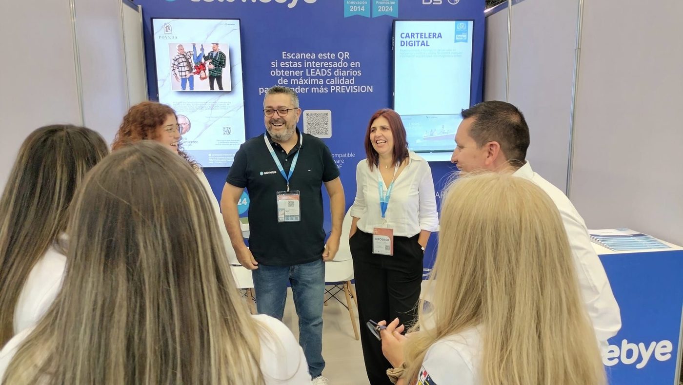 Estand de Tellmebye en FUMEXPO 2024, con la cartelera digital en pantalla y el equipo conversando con visitantes.
