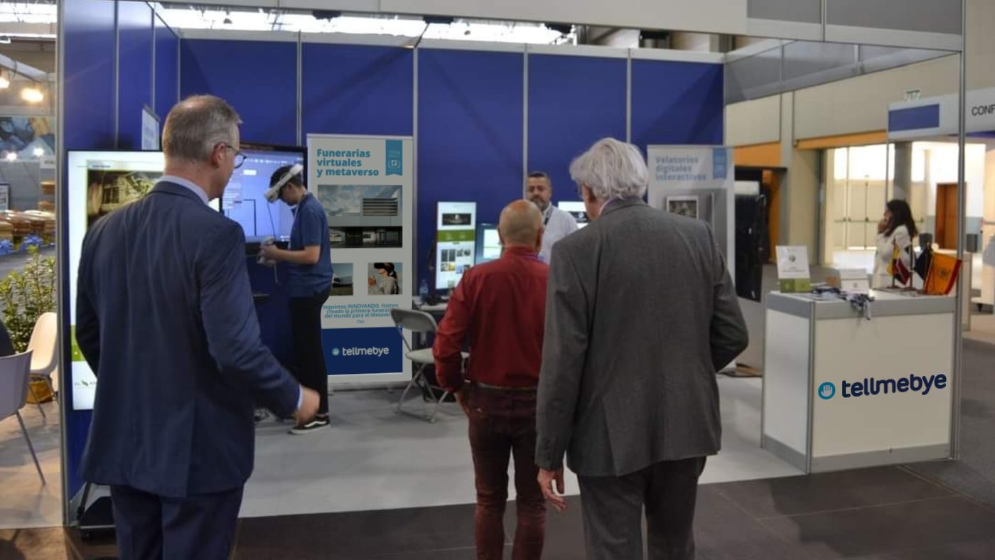 Estand de Tellmebye en Funergal 2022: un visitante prueba las gafas de realidad virtual junto al cartel de funerarias virtuales y metaverso.